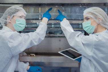 Kadın fabrika işçileri endüstriyel fabrikadaki makine sistemlerini kontrol ediyorlar. Kadınlar içecek ve gıda üretimi için temiz odalarda çalışıyorlar