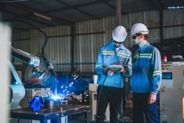 Fabrika mühendisleri, metal levhaları kesmek için kol robotu makinesini kontrol etmek için akıllı kontrol kullanıyor. Uzman işçiler, elektronik parçayı üretmek için yükseklik teknolojisi sektöründe çalışıyorlar..