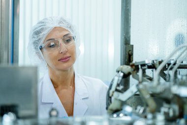 Makinedeki su dağıtıcısını kontrol eden fabrika kadın mühendisi. İşçi endüstriyel fabrikanın makine taşıma hattındaki su şişelerinin kalitesini kontrol eder..