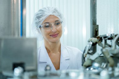 Makinedeki su dağıtıcısını kontrol eden fabrika kadın mühendisi. İşçi endüstriyel fabrikanın makine taşıma hattındaki su şişelerinin kalitesini kontrol eder..