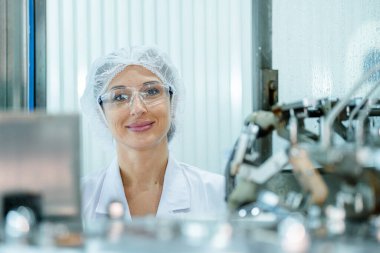 Makinedeki su dağıtıcısını kontrol eden fabrika kadın mühendisi. İşçi endüstriyel fabrikanın makine taşıma hattındaki su şişelerinin kalitesini kontrol eder..