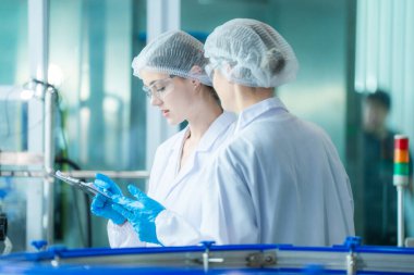 Bilim adamı, endüstriyel fabrikanın makine taşıma hattındaki su şişelerinin kalitesini kontrol ediyor. İçki üretim hattında veri kaydeden kadın işçi..