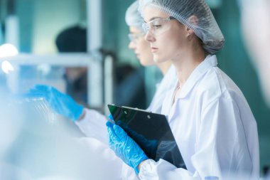 Bilim adamı, endüstriyel fabrikanın makine taşıma hattındaki su şişelerinin kalitesini kontrol ediyor. İçki üretim hattında veri kaydeden kadın işçi..