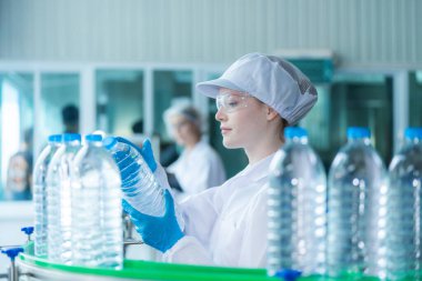 Bilim adamı, endüstriyel fabrikanın makine taşıma hattındaki su şişelerinin kalitesini kontrol ediyor. İçki üretim hattında veri kaydeden kadın işçi..