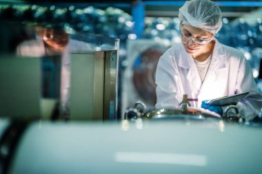 Fabrika işçisi endüstriyel fabrikadaki depoda su şişelerini kontrol ediyor. İçki üretim hattında veri kaydeden kadın işçi..