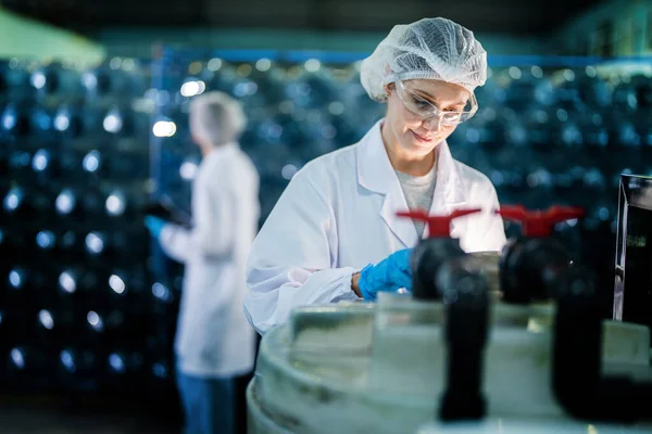 工場で倉庫内のウォーターボトルをチェックする工場労働者 飲料製造ラインでデータを記録する女性労働者 — ストック写真