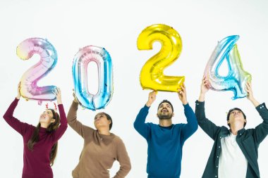Bir grup insan yeni yıl için 2024 sayısının fantezi renkli balonlarını tutuyor. Beyaz arka planda duran kadın ve erkekler. Mutlu yıllar partisi.