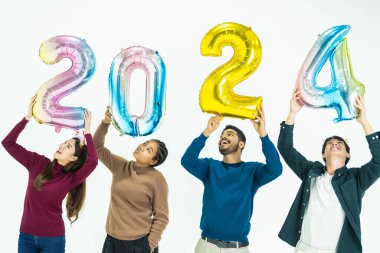 Bir grup insan yeni yıl için 2024 sayısının fantezi renkli balonlarını tutuyor. Beyaz arka planda duran kadın ve erkekler. Mutlu yıllar partisi.