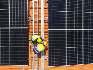 Üst düzey mühendisler çatıdaki güneş pili paneli veya fotovoltaik hücrenin yapımını denetliyor. Yeşil enerjinin endüstriyel yenilenebilir enerjisi. Kentsel alanda bir fabrika. İşçi kule çatısında çalışıyor..
