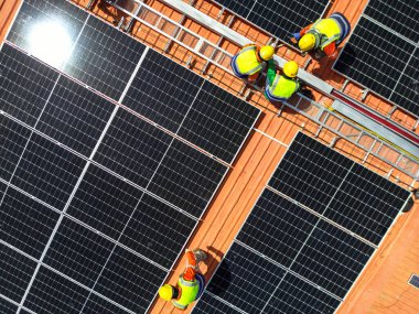 Üst düzey mühendisler çatıdaki güneş pili paneli veya fotovoltaik hücrenin yapımını denetliyor. Yeşil enerjinin endüstriyel yenilenebilir enerjisi. Kentsel alanda bir fabrika. İşçi kule çatısında çalışıyor..