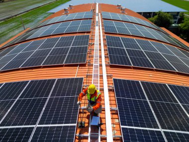 Mühendis çatıdaki güneş pili panelinin veya fotovoltaik hücrenin yapımını denetliyor. Yeşil enerjinin endüstriyel yenilenebilir enerjisi. Kentsel alanda bir fabrika. İşçi kule çatısında çalışıyor..