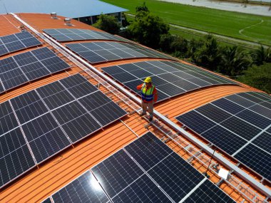 Mühendis çatıdaki güneş pili panelinin veya fotovoltaik hücrenin yapımını denetliyor. Yeşil enerjinin endüstriyel yenilenebilir enerjisi. Kentsel alanda bir fabrika. İşçi kule çatısında çalışıyor..