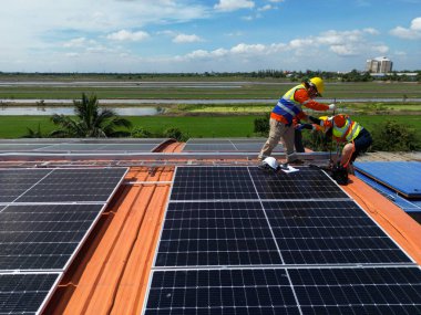 Mühendis çatıdaki güneş pili panelinin veya fotovoltaik hücrenin yapımını denetliyor. Yeşil enerjinin endüstriyel yenilenebilir enerjisi. Kentsel alanda bir fabrika. İşçi kule çatısında çalışıyor..