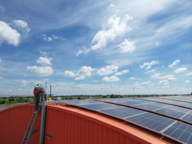 Mühendis çatıdaki güneş pili panelinin veya fotovoltaik hücrenin yapımını denetliyor. Yeşil enerjinin endüstriyel yenilenebilir enerjisi. Kentsel alanda bir fabrika. İşçi kule çatısında çalışıyor..