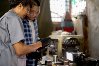 Adamlar makine yerleştirmek için çelik parçaları inceliyor. Öğretmen ve öğrenci takımı çelik fabrikasında ağır makineler kullanmayı öğreniyor. İşçiler üretim sırasında kalite kontrolü yaparken işbirliği yaparlar.