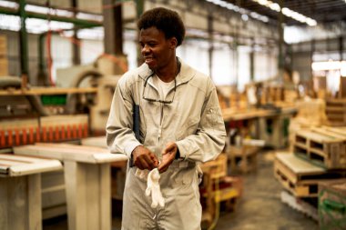 Afrikalı işçiler, makine dairesinde çalışan süit elbisesi ve eldiveni ile özgüvenle ayakta duruyorlar. Akıllı endüstri çalışanı kavramı. Ahşap fabrikası ağaç damak üretir.