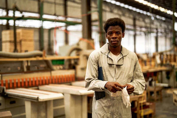 African man workers engineering standing with confidence with working suite dress and hand glove in front machine. Concept of smart industry worker operating. Wood factory produce wood palate.