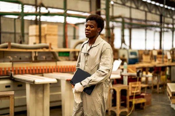 African man workers engineering standing with confidence with working suite dress and hand glove in front machine. Concept of smart industry worker operating. Wood factory produce wood palate.