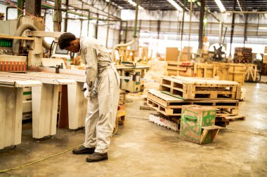 Afrikalı işçiler, makine dairesinde çalışan süit elbisesi ve eldiveni ile özgüvenle ayakta duruyorlar. Akıllı endüstri çalışanı kavramı. Ahşap fabrikası ağaç damak üretir.