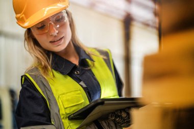 Marangoz kadın güvenlik üniforması ve şapka takıyor atölyedeki ahşap ürünlerin kalitesini kontrol ediyor. Erkek ve kadın işçiler karanlık depo endüstrisinde ahşap..