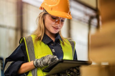 Marangoz kadın güvenlik üniforması ve şapka takıyor atölyedeki ahşap ürünlerin kalitesini kontrol ediyor. Erkek ve kadın işçiler karanlık depo endüstrisinde ahşap..