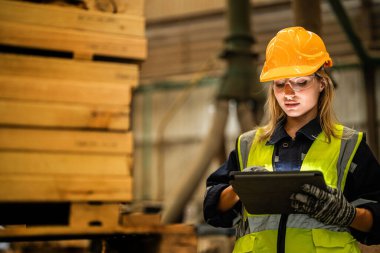 Marangoz kadın güvenlik üniforması ve şapka takıyor atölyedeki ahşap ürünlerin kalitesini kontrol ediyor. Erkek ve kadın işçiler karanlık depo endüstrisinde ahşap..