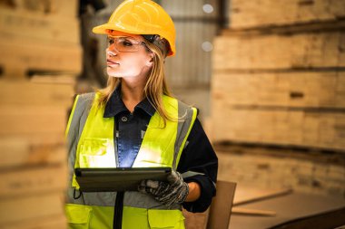 Marangoz kadın güvenlik üniforması ve şapka takıyor atölyedeki ahşap ürünlerin kalitesini kontrol ediyor. Erkek ve kadın işçiler karanlık depo endüstrisinde ahşap..