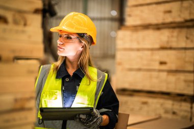 Marangoz kadın güvenlik üniforması ve şapka takıyor atölyedeki ahşap ürünlerin kalitesini kontrol ediyor. Erkek ve kadın işçiler karanlık depo endüstrisinde ahşap..