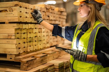 Marangoz kadın güvenlik üniforması ve şapka takıyor atölyedeki ahşap ürünlerin kalitesini kontrol ediyor. Erkek ve kadın işçiler karanlık depo endüstrisinde ahşap..