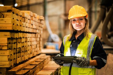 Marangoz kadın güvenlik üniforması ve şapka takıyor atölyedeki ahşap ürünlerin kalitesini kontrol ediyor. Erkek ve kadın işçiler karanlık depo endüstrisinde ahşap..