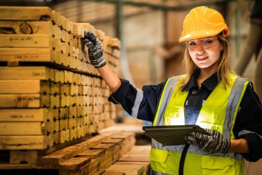Marangoz kadın güvenlik üniforması ve şapka takıyor atölyedeki ahşap ürünlerin kalitesini kontrol ediyor. Erkek ve kadın işçiler karanlık depo endüstrisinde ahşap..