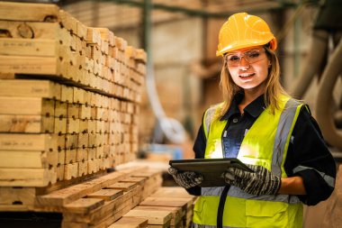 Marangoz kadın güvenlik üniforması ve şapka takıyor atölyedeki ahşap ürünlerin kalitesini kontrol ediyor. Erkek ve kadın işçiler karanlık depo endüstrisinde ahşap..