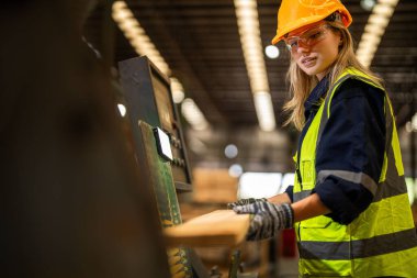 Fabrika mühendisi kadın kontrol paneli anahtarı için kendinden emin duruyor. İşçi, sanayi fabrikasındaki ağır makinede çalışıyor. İşçi, ham ahşap kerestelerini kontrol ediyor. akıllı endüstri çalışanı.