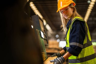 Fabrika mühendisi kadın kontrol paneli anahtarı için kendinden emin duruyor. İşçi, sanayi fabrikasındaki ağır makinede çalışıyor. İşçi, ham ahşap kerestelerini kontrol ediyor. akıllı endüstri çalışanı.