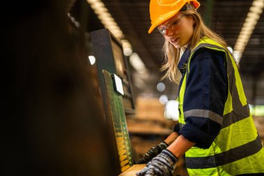 Fabrika mühendisi kadın kontrol paneli anahtarı için kendinden emin duruyor. İşçi, sanayi fabrikasındaki ağır makinede çalışıyor. İşçi, ham ahşap kerestelerini kontrol ediyor. akıllı endüstri çalışanı.