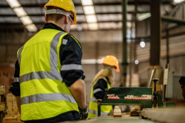 Karanlık depo endüstrisinde kereste temizleyen bir adam. Takım çalışanı marangoz, güvenlik üniforması ve şapka takıyor atölyede ahşap ürünlerin kalitesini kontrol ediyor ve çalışıyor..