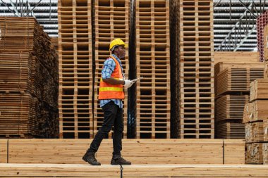 Afrikalı işçiler, kereste deposunda çalışan süit elbise ve eldiven ile yürüyen ve denetleyen mühendisler. Akıllı endüstri çalışanı kavramı. Ahşap fabrikaları ağaç damak üretir..