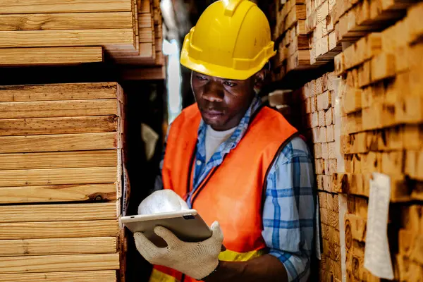 アフリカの労働者カーペンターは 安全制服とハードハットの作業を着て ワークショップ製造で木製品の品質をチェックしています ダークウェアハウス産業の男女労働者 — ストック写真