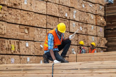 Afrikalı işçiler, kereste deposunda çalışan süit elbise ve eldiven ile yürüyen ve denetleyen mühendisler. Akıllı endüstri çalışanı kavramı. Ahşap fabrikaları ağaç damak üretir..