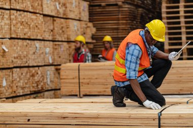 Afrikalı işçiler, kereste deposunda çalışan süit elbise ve eldiven ile yürüyen ve denetleyen mühendisler. Akıllı endüstri çalışanı kavramı. Ahşap fabrikaları ağaç damak üretir..
