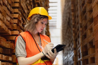 Marangoz kadın güvenlik üniforması ve şapka takıyor atölyedeki ahşap ürünlerin kalitesini kontrol ediyor. Erkek ve kadın işçiler karanlık depo endüstrisinde ahşap..