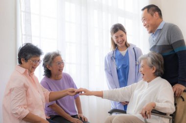 Asyalı genç hemşire, yaşlı ve tekerlekli sandalyedeki yaşlı erkek ve kadını destekliyor. Yaşlı olgun ve hastanede yaşayan bir grup kıdemli arkadaş. Emekli insanların sosyalleşmesi.