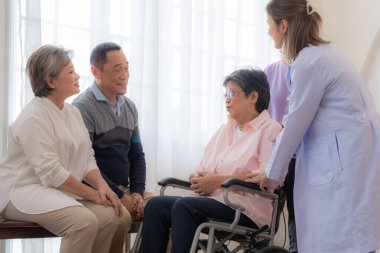 Tekerlekli sandalyedeki yaşlı kadın için Asyalı genç hemşire desteği. Yaşlı olgun ve hastanede yaşayan bir grup kıdemli arkadaş. Emekli insanların sosyalleşmesi.