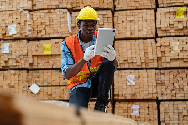 African workers man engineering walking and inspecting with working suite dress and hand glove in timber wood warehouse. Concept of smart industry worker operating. Wood factories produce wood palate.
