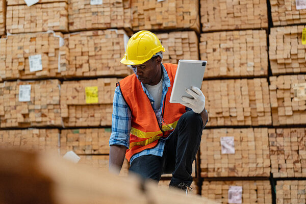 African workers man engineering walking and inspecting with working suite dress and hand glove in timber wood warehouse. Concept of smart industry worker operating. Wood factories produce wood palate.