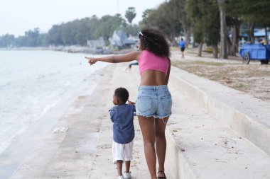 Karışık ırk Afrikalı ve Asyalı anne ve çocuk açık havada oynuyorlar. Gülümseyen mutlu aile kumsalda koşarken iyi eğlenceler. Anne ve çocuğun eşsiz bir saç stili olan portresi..