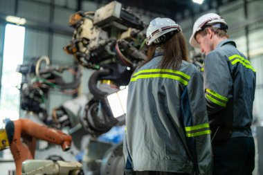 Mühendisler ağır makine robot kolunu kontrol ediyorlar. Çeşitli Endüstriyel Robot Mühendisleri Ekibi Makine etrafında toplandı. Profesyonel Makine İşlemcileri elektrikli robotu parlak dijital panelde tamir ederler.