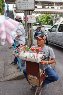 Bangkok, Tayland - 8 Temmuz 2013: Bangkok kaldırımında renkli lolipop ve geleneksel şekerleme satan bir Tayland sokak satıcısı. Yakınlarda bir başka satıcı çubukta pamuk şeker torbası taşıyor..