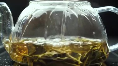 Çaydanlıktaki yeşil çay yaprağı kaynatılmış ve koyu arkaplanda sıcak su ile doldurulmuş.