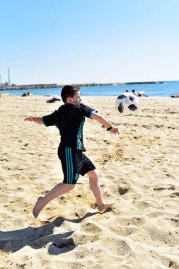 Çocuk plajda futbol oynuyor. 